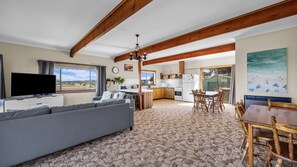 A spacious living area with a sofa, a dining table with chairs, a kitchen area, and a large window offering a view of the outdoors.