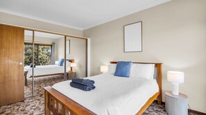 A hotel room with a bed, a bedside table with a lamp, a mirror, and a view through a door.