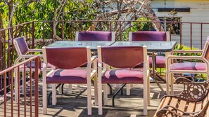 Une terrasse extérieure avec des tables et des chaises, entourée d’une clôture en métal et de verdure.