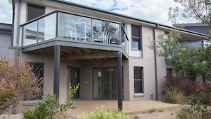 A modern two-story building with a glass balcony, a covered entrance, and a landscaped garden area.