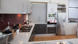 A modern kitchen with grey cabinets, a stainless steel refrigerator, and a built-in oven. - Moorhen Cove 3 - Unit 3 Wallaga Lake Rd 15 (BERMAGUI)