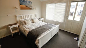 A bedroom with a bed, bedside tables, a nightstand, a window with blinds, and a door.