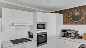 A modern kitchen with white cabinets, a microwave, oven, and a coffee machine.