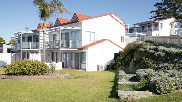 A modern two-story residential building with a red-tiled roof, large windows, and a balcony.