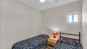 Une chambre avec deux lits simples, une table de chevet avec une lampe, une fenêtre et un ventilateur de plafond.