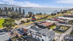 Vista aérea de un pueblo costero con un letrero destacado de SCA South Coast Accommodation, que muestra una combinación de edificios residenciales y comerciales, un área de estacionamiento y vistas al mar.