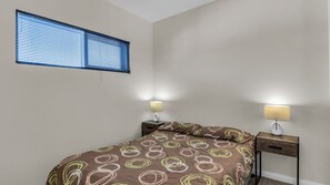 Un dormitorio con una cama, dos mesitas de noche, una ventana con persianas y dos lámparas de pared.