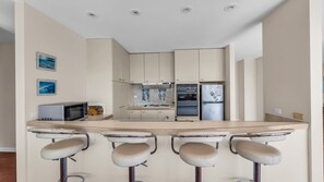Una cocina moderna con una isla central, taburetes de bar, un microondas, una estufa y un refrigerador.