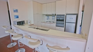 Eine moderne Küche mit Kochinsel, Barhocker, Mikrowelle, Wasserkocher und Kühlschrank.