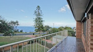 A balcony with a view of the sea, a grassy area, and a brick building. - Gull Cottage - Pacific Drive 7 (BERMAGUI)