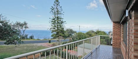 A balcony with a view of the sea, a grassy area, and a brick building.