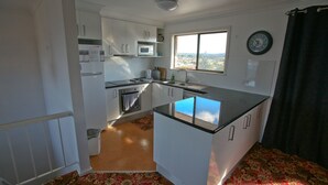 A compact kitchen with white cabinets, a microwave, a sink, and a window with a view. - Gull Cottage - Pacific Drive 7 (BERMAGUI)