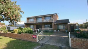 A two-story residential building with a balcony, a gated driveway, and a sign indicating holiday rental availability. - Gull Cottage - Pacific Drive 7 (BERMAGUI)