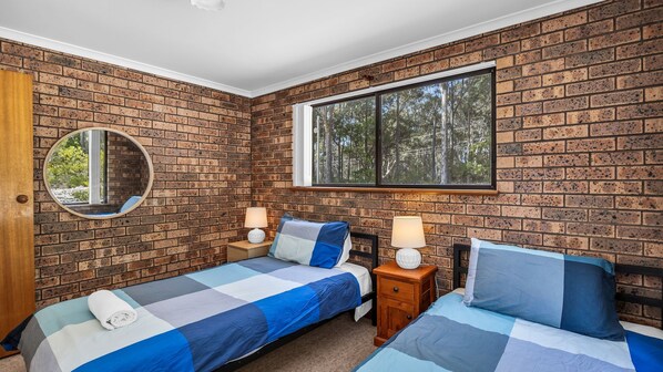 A bedroom with two beds, a large window, a mirror, and a brick wall.