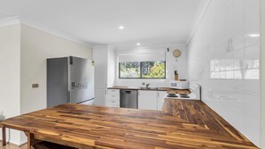A modern kitchen with a wooden countertop, stainless steel appliances, and a window with a view of greenery.