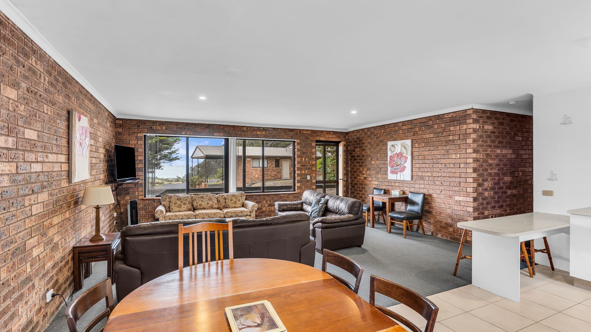 A spacious living area with a brick wall, a large window, a sofa, a leather couch, and a dining table with chairs.