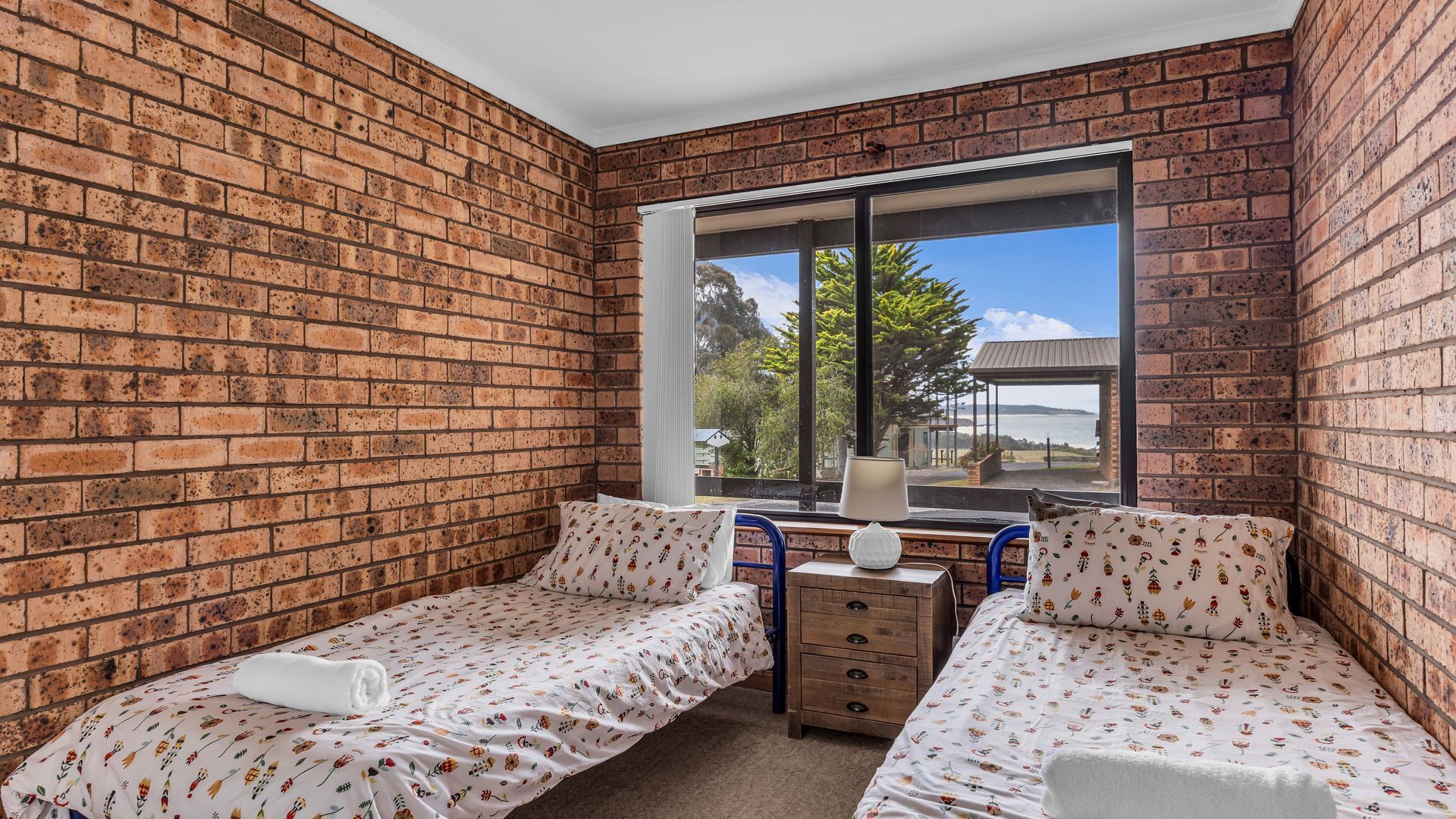 Une chambre avec deux lits simples, une fenêtre donnant sur un paysage agréable et un mur en briques.