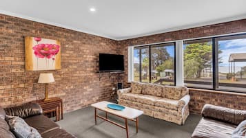 A living room with a brick wall, a sofa, a coffee table, a TV, and a large window with a view of the outdoors.