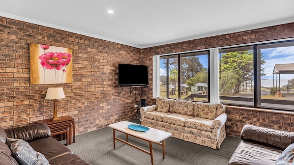 A living room with a brick wall, a sofa, a coffee table, a TV, and a large window with a view of the outdoors.