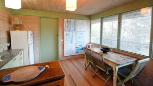 A compact kitchen with a wooden table, chairs, a refrigerator, and a window with a view of trees.