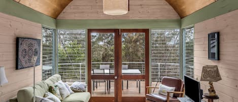 Un intérieur chaleureux avec un plafond en bois, un canapé, un fauteuil, une table et un téléviseur.