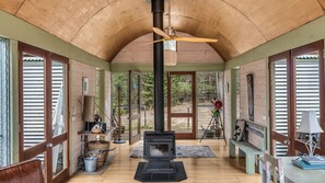 A cozy room with a wooden ceiling, a black wood stove, and a ceiling fan.