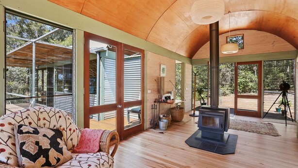 A spacious room with a large wooden ceiling, a built-in fireplace, and large windows offering views of the outdoors.