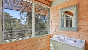 A wooden cabin bathroom with a large window, a sink, and a mirror.