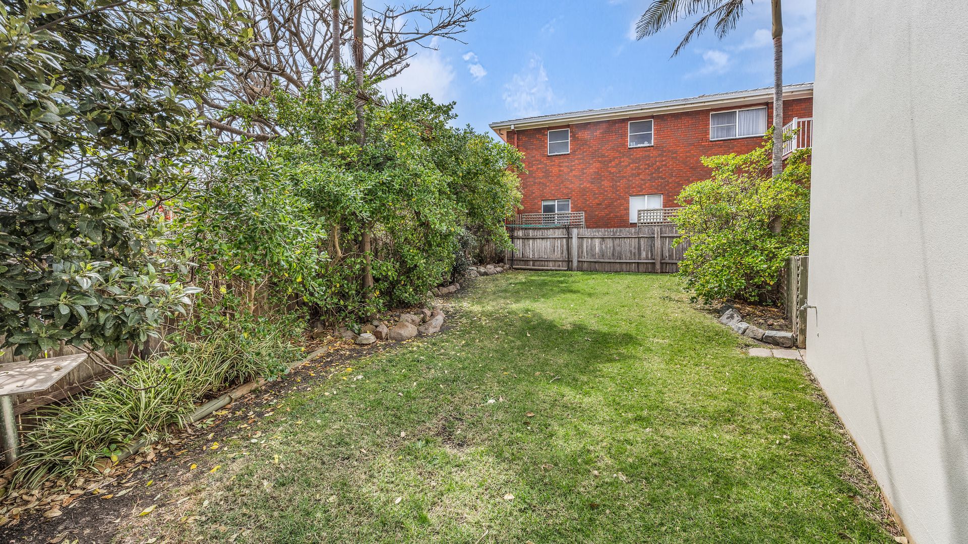A backyard with a grassy lawn, a wooden fence, and a red brick building in the background.
