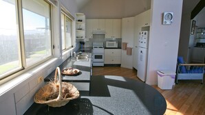 Une cuisine de taille réduite avec des meubles blancs, un four à micro-ondes, une cuisinière et un réfrigérateur. Il y a une fenêtre sur le côté gauche, une poubelle et une chaise bleue dans le coin.