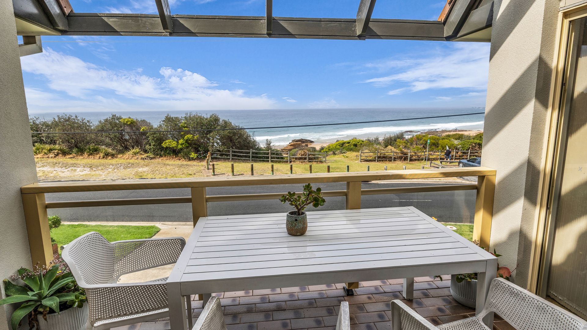 A balcony with a view of the ocean, a table with a potted plant, and outdoor seating.