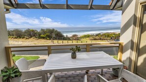 A balcony with a view of the ocean, a table with a potted plant, and outdoor seating.