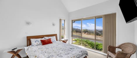 A bedroom with a large bed, a chair, and a TV mounted on the wall.