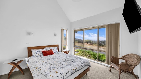 A bedroom with a large bed, a chair, and a TV mounted on the wall.