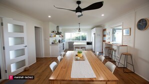 A modern kitchen with white cabinets, a wooden dining table, and a ceiling fan. - Blue Pool Hideaway - Scenic Drive 7 (Bermagui)
