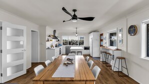 Una cocina moderna con armarios blancos, una isla central y un comedor con mesa de madera y sillas blancas.
