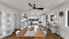 Een moderne keuken met witte kastjes, een centraal eiland en een eetgedeelte met een houten tafel en witte stoelen.
