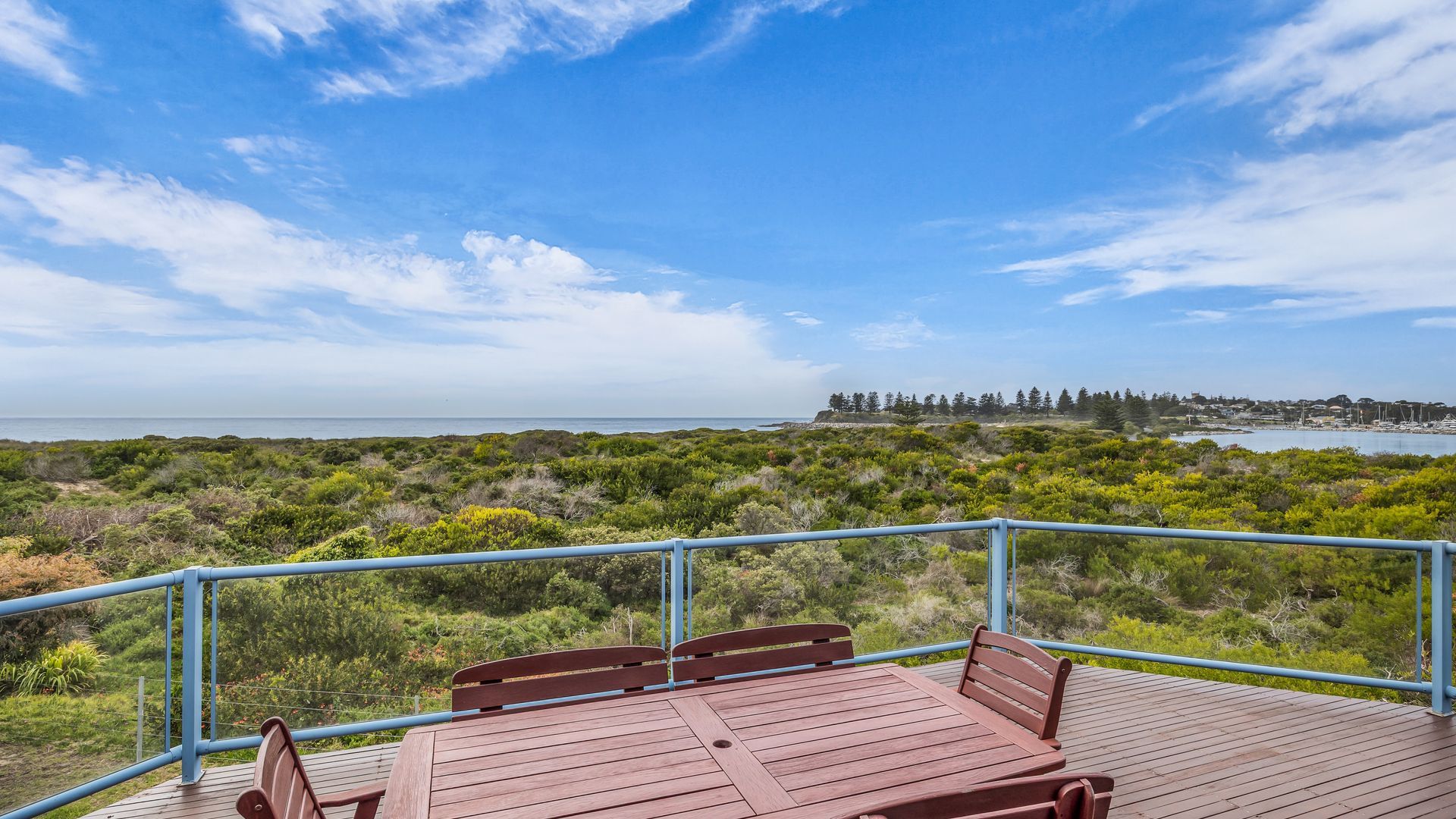 Une terrasse en bois dotée d’une rambarde, offrant une vue sur un paysage côtier caractérisé par une végétation luxuriante et une ligne de côte lointaine.