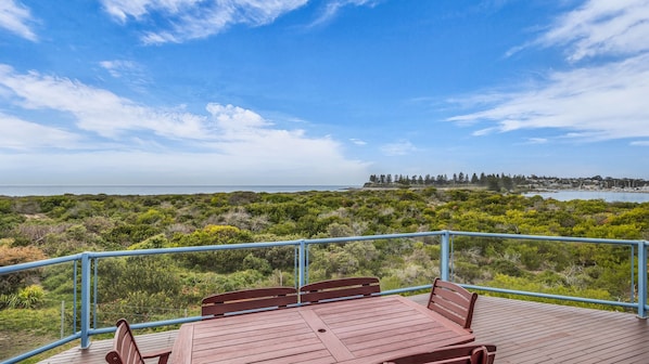 A wooden deck with a railing, overlooking a coastal landscape with dense vegetation and a distant shoreline.