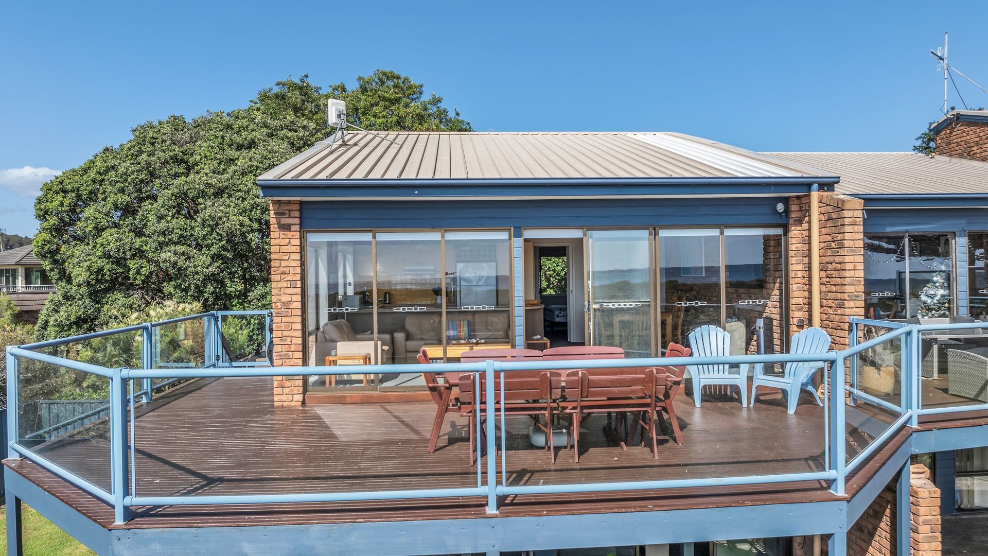 A house with a deck, a dining area with chairs, and a large window.