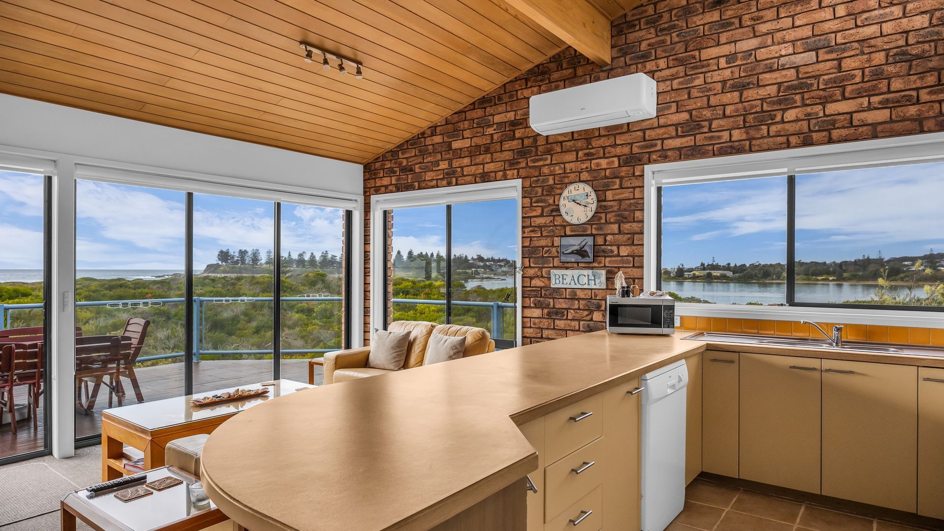 A kitchen with a view of a lake, a clock, and a sign that says 'BEACH'.