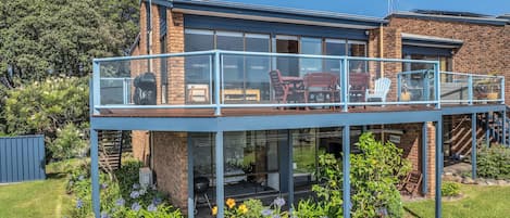 A two-story house with a glass balcony, outdoor seating, and a garden.