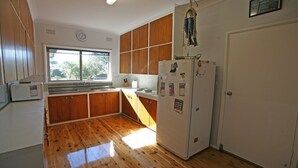 Une cuisine avec des meubles de rangement en bois, un réfrigérateur, un évier et une fenêtre donnant sur des arbres.