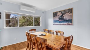 A dining room with a wooden table and chairs, a window with blinds, and a poster on the wall.