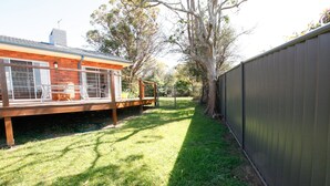 A backyard with a wooden deck, a fenced area, and a large tree.