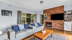 A living room with a grey sofa, a wooden coffee table, a brick fireplace, a mounted TV, and a bookshelf.