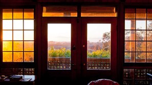 Um quarto com uma grande porta de madeira com painéis de vidro, vista para uma paisagem com árvores e grama, e uma mesa com objetos sobre ela.