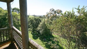 Une terrasse en bois dotée d’une rambarde en treillis, qui offre une vue sur un paysage verdoyant et luxuriant, avec des arbres et des collines.