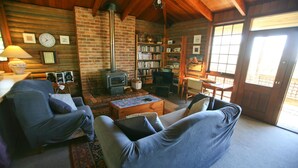 Un intérieur de chalet chaleureux avec une cheminée, des étagères à livres, un téléviseur et des sièges confortables.