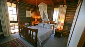 Une chambre située dans une cabane en rondins, avec un lit à baldaquin, des lampes de chevet, une bibliothèque et une grande fenêtre avec des rideaux.